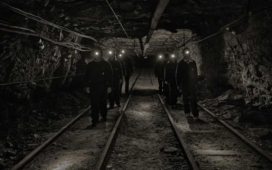 Miners with head torches walking down a dark tunnel along narrow rails