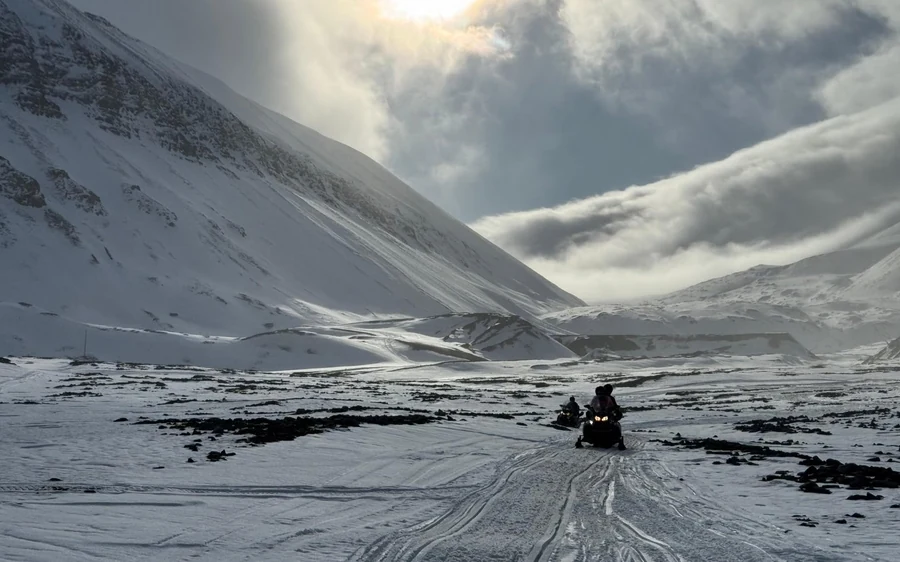 A snowmobile crossing a wide snow-covered valley under dark mountains