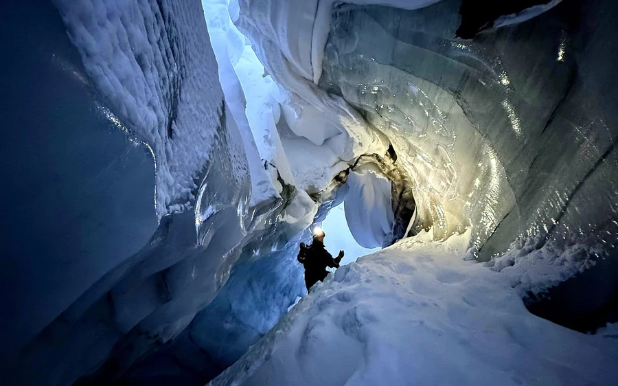 A figure standing under a low arch at the entrance to a glacier ice cave