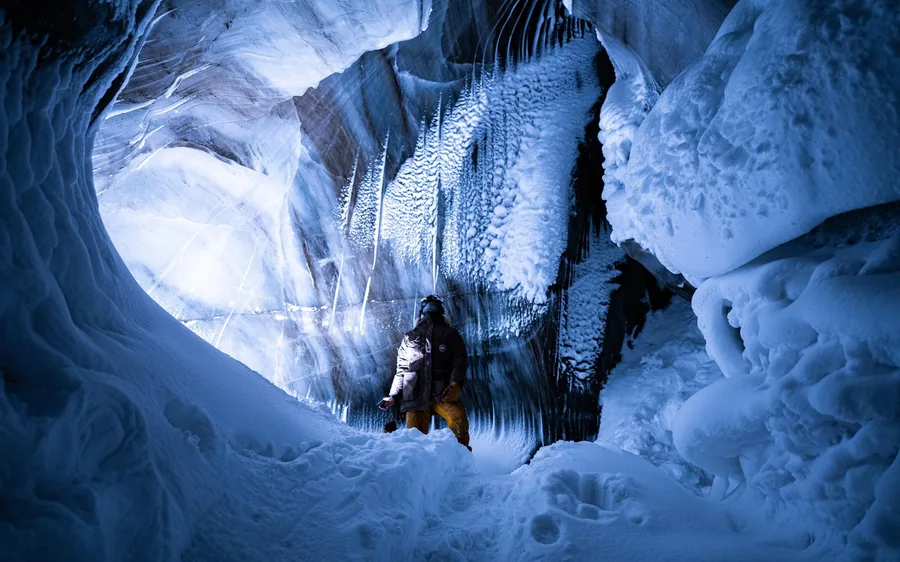 A person in a snowsuit standing in a wide chamber of blue and white glacier ice