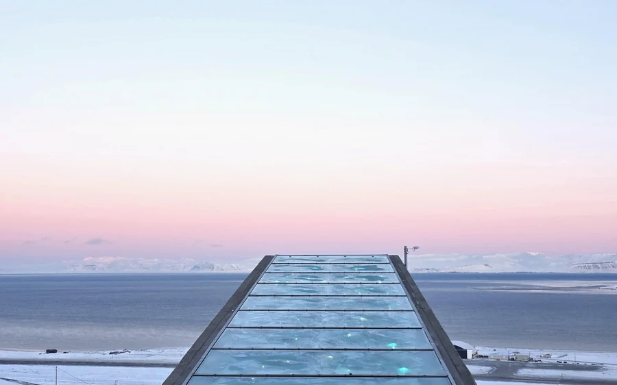 The glass and steel roof of the Seed Vault entrance against a pale pink Arctic sky