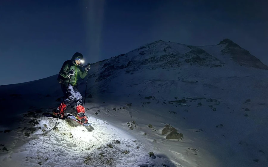 A hiker with a head torch climbing a dark snowy slope at night