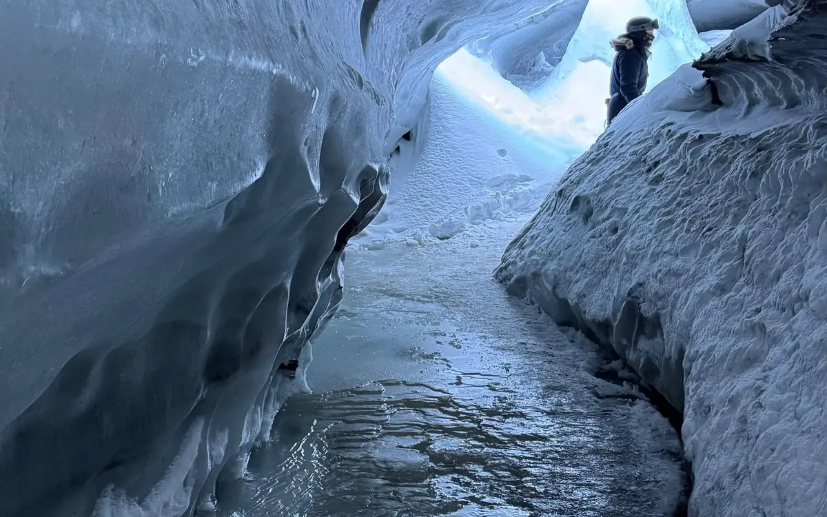 Blue ice and meltwater shapes inside a glacier chamber lit by a headlamp